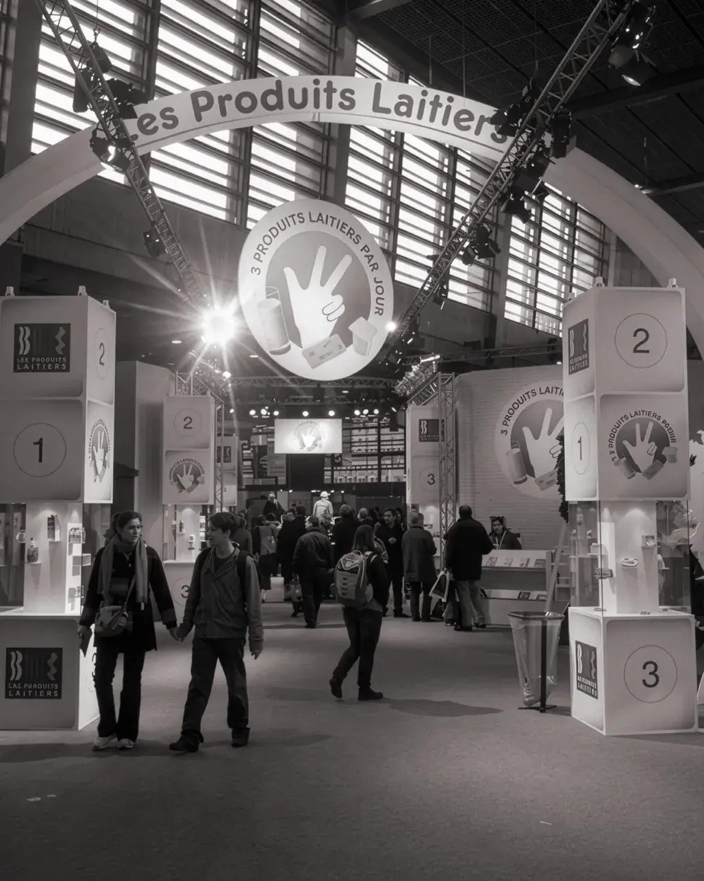 Stand ouvert avec grandes colonnes intégrant des vitrines et une enseigne haute ronde Les Produits Laitiers. (NB)